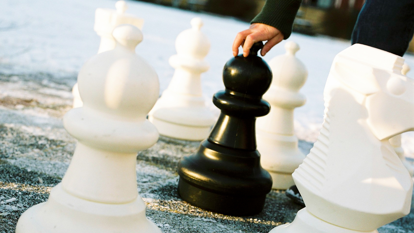 Hand sträcker sig efter stor schackpjäs i utomhusmiljö.