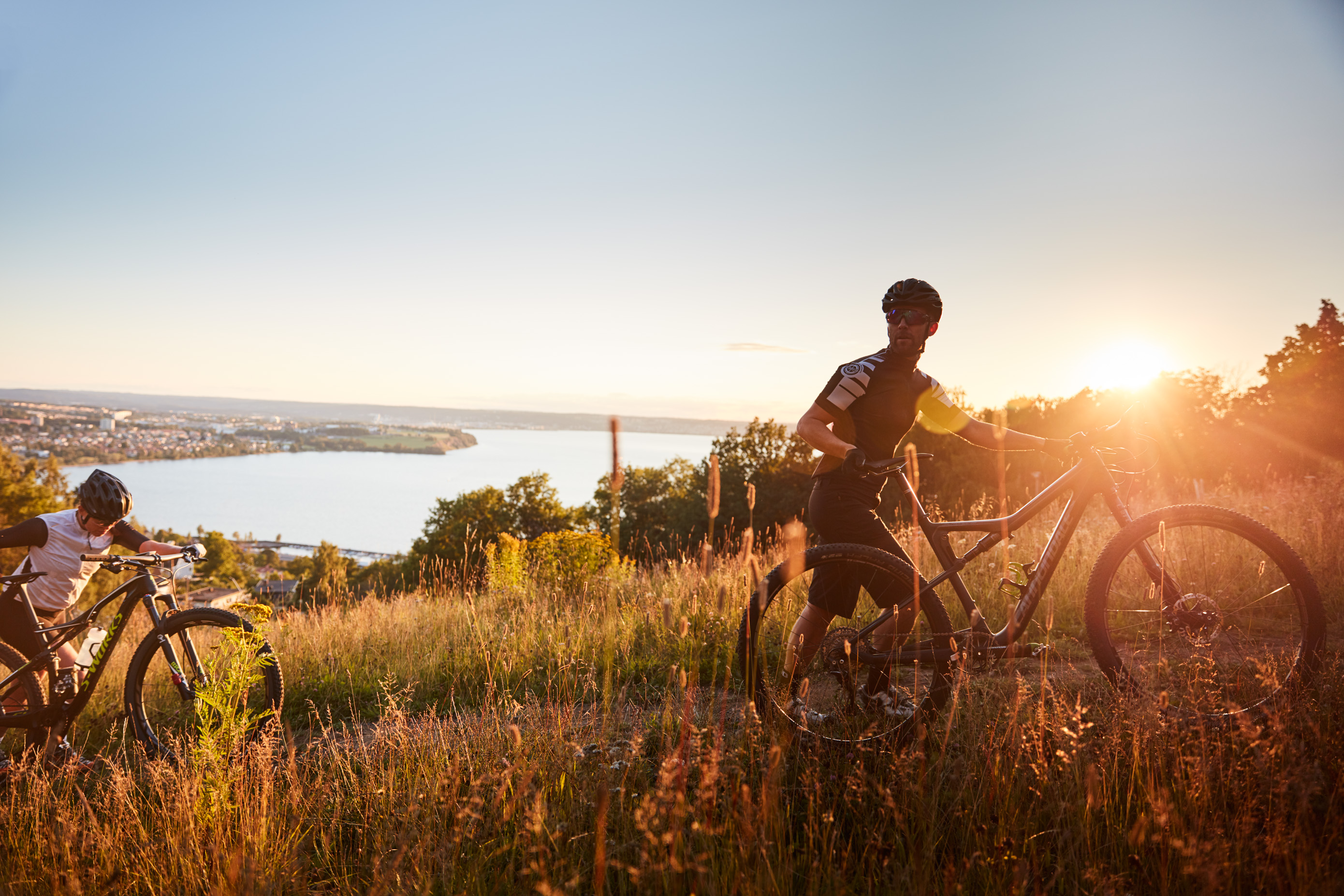 Visar två människor som leder sina cyklar uppför ett berg med utsikt över en sjö i solnedgång.