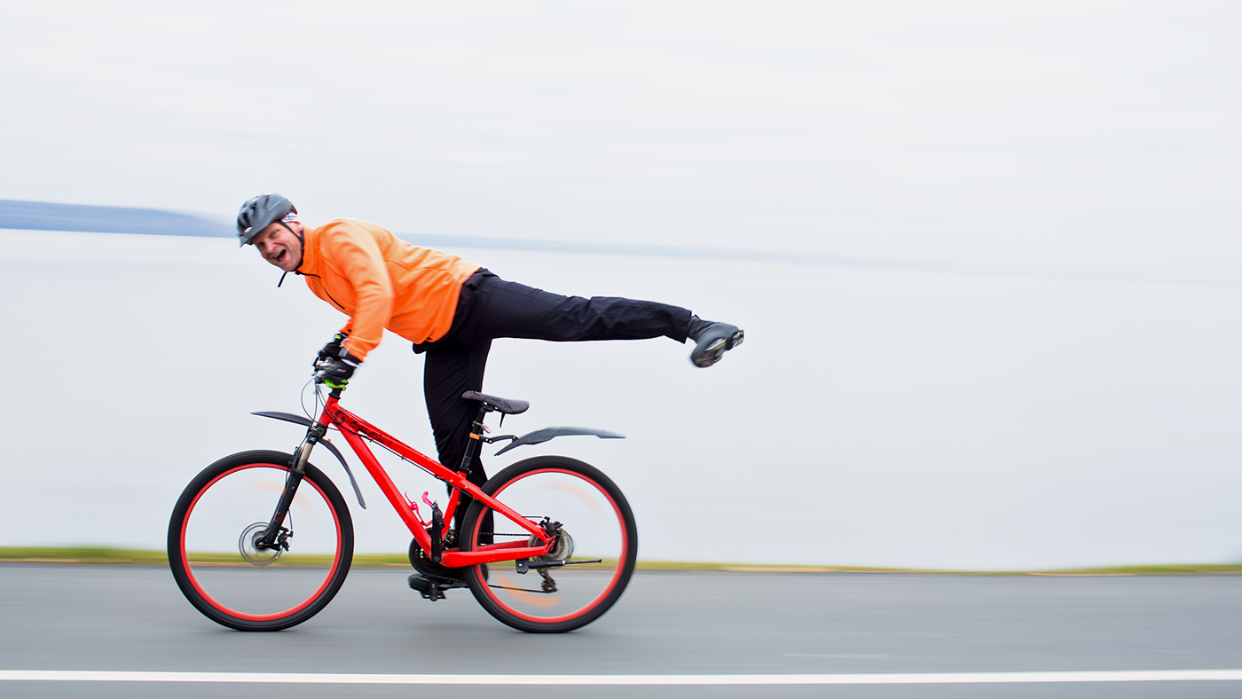 Man på cykel gör tokig min och akrobatisk pose genom att stå på bara en pedal och hålla det andra benet över bakhjulet.